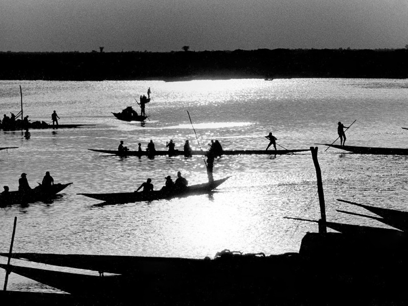Mali, Mopti. 1986. Rowers navigate their canoes with cargo and passengers across the river Niger at sunset.